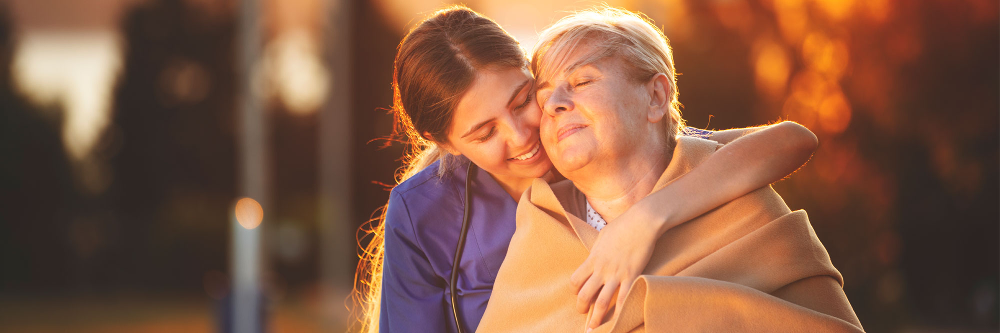 Warm blanket wrapped around senior woman by a young female medical provider.