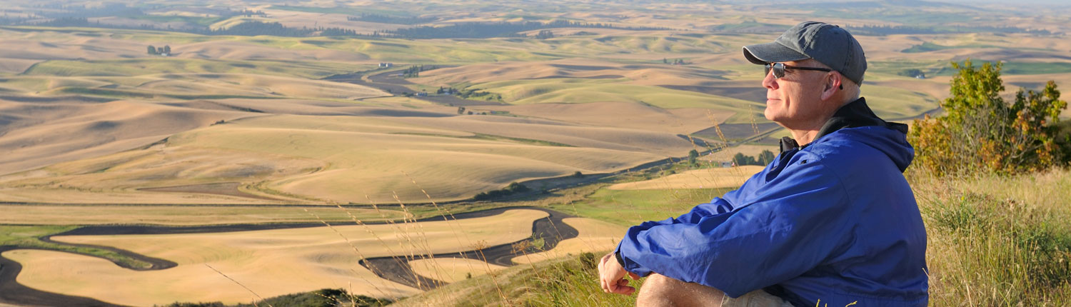 Senior man staring while sitting down on a grassy hill